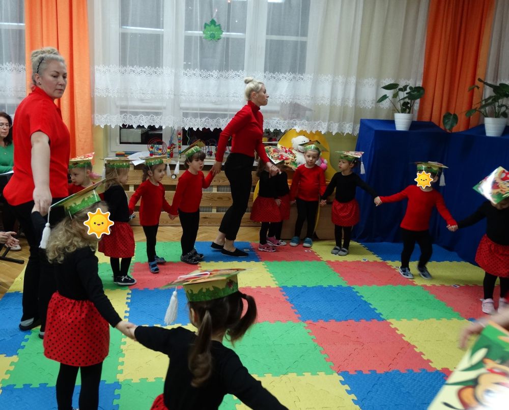Dzieci ubrane w stroje biedronek, tańczą w kole ze swoimi Paniami