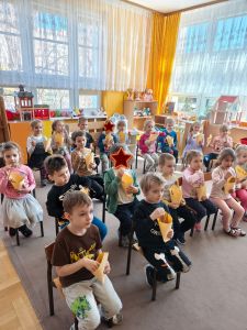 Dzieci siedzą na krzesełkach i oglądają bajkę