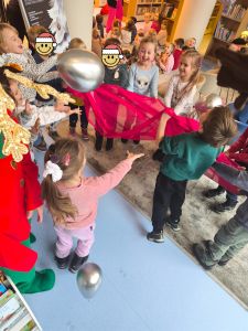 Dzieci stoją w kole, trzymają czerwoną chustkę na której odbijają balon.