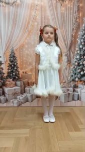 Dziewczynka w stroju śnieżynki stoi a za nią jest świąteczne tło
