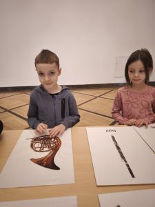 Chłopiec i dziewczynka stoją przy stole a przed nimi leżą karty z obrazkami instrumentów