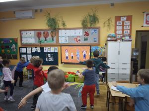 Dzieci tańczą zumbę na dywanie naśladując ruchy postaci z telewizora