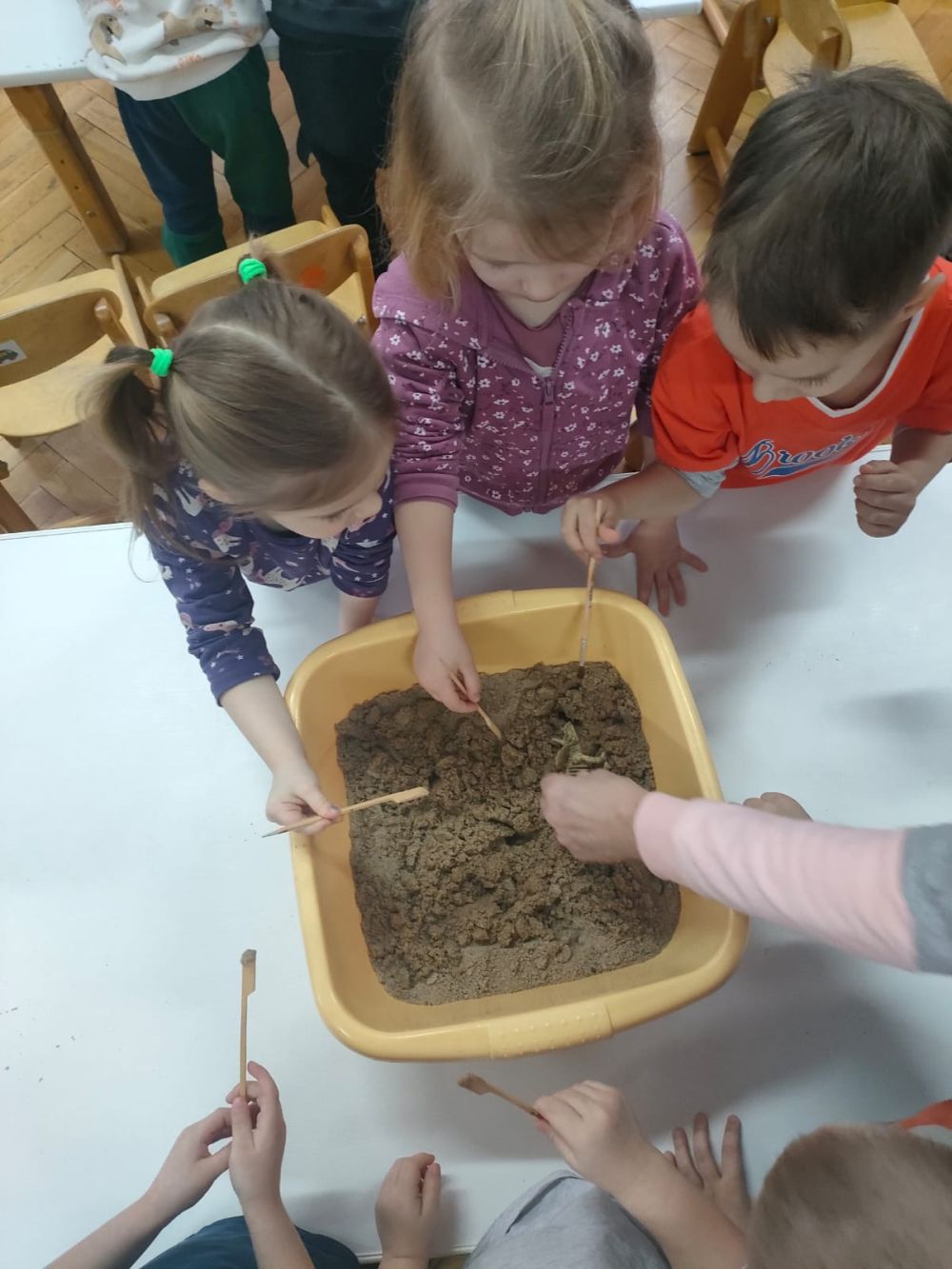 Dzieci szukają dinozaurów w miskach z pisakiem.