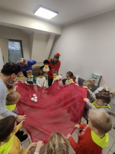 Dzieci trzymają czerwoną chustę i podrzucają styropianowe kulki