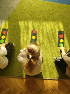 Dzieci siedzą w kole a przed nimi leży prostokątna kartka i kolorowe kółka z papieru