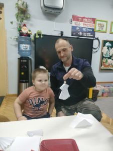 Chłopiec siedzi obok swojego Taty. Tata pokazuje zrobionego z papieru Aniołka