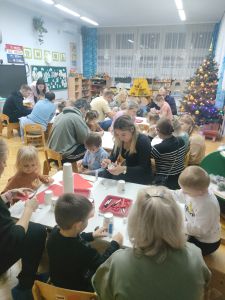 Rodzice z dziećmi siedzą przy stolikach i robią świąteczne ozdoby