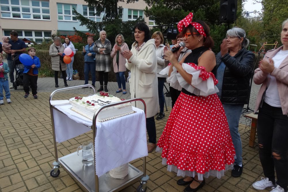 Pracownicy przedszkola, rodzice i dzieci, Pani dyrektor i Pani w stroju myszki mini stoją na placu zabaw. przed nimi stoi Tort