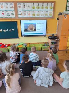 Dzieci siedzą na dywanie i oglądają film o kleszczach