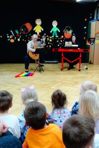 Pani gra na gitarze a druga na kibordzie. Dzieci patrzą siedząc na dywanie