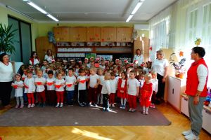 Dzieci i Pani z całego przedszkola ubrane w biało czerwone stroje stoją i śpiewają Hymn