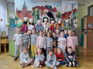 Zdjęcie grupowe grupy 3. W tle dekoracja z przedstawienia- kukiełki i namalowane miasto