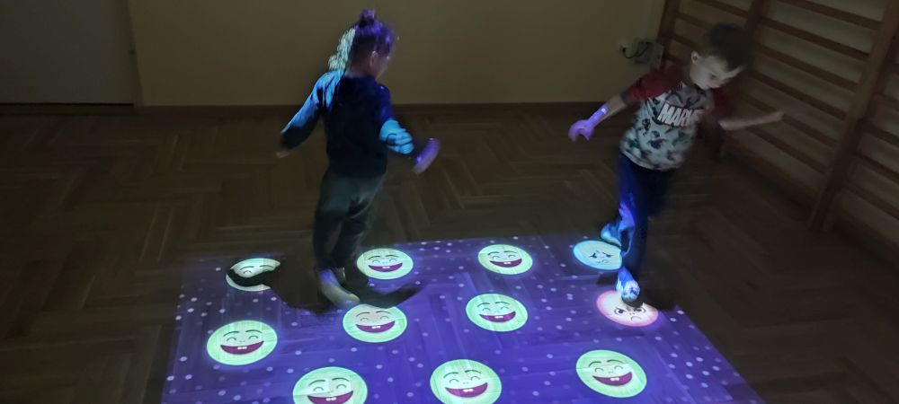 Chłopiec i dziewczynka bawią się na magicznym dywanie, nadeptując na wyświetlane smutne buźki