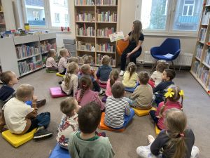 dzieci siedzą na podłodze i słuchają pani która siedzi i czyta książkę