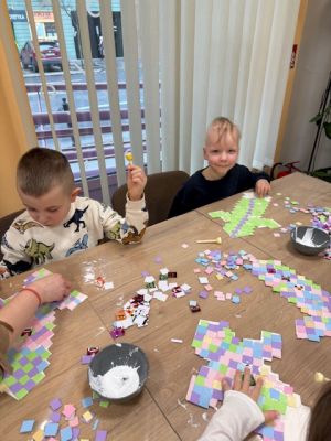 Dwóch chłopców siedzi przy stole i wyklejają kwadracikami kartonowy miecz dobra