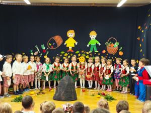 Dzieci stoją w półkolu. Ubrane są w ludowe stroje.