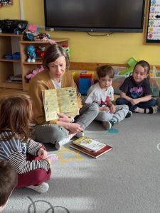 Dzieci siedzą na dywanie i słuchają mamy stefana która czyta książkę