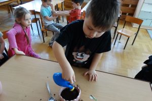 Chłopiec podlewa konewką posadzone w doniczce roślinki