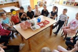 Dzieci siedzą dookoła stolika na którym leżą przygotowane rzeczy do siania i sadzenia 