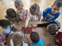 Dziewczynka wsypuje ziarenka do foremki, a inne dzieci stoją przy stoliku i patrzą