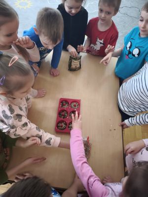 dzieci wsypują ziarenka do foremki, inne dzieci stoją wokół stolika