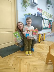 Mama i chłopiec pokazują zrobione prace: kartka z zajączkiem, zajączek z papierowego talerzyka, jajko z papierowych pasków