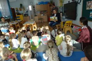 Dzieci siedzą na dywanie i słuchają książki czytanej przez Panią Burmistrz