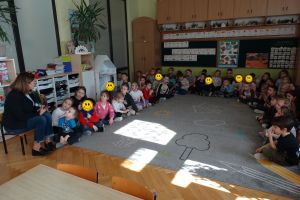 Dzieci siedzą na dywanie i słuchają książki czytanej przez Panią Burmistrz