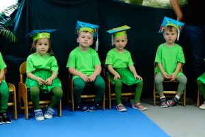 Dzieci ubrane na zielono siedzą na krzesełkach